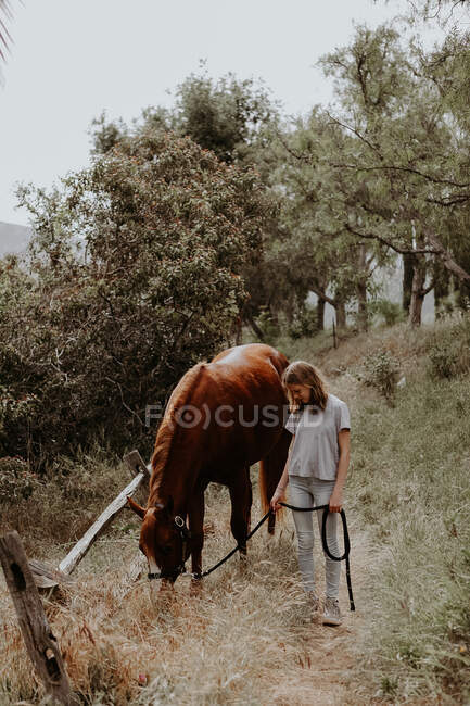 Girl standing next to a grazing horse, California, USA — Stock Photo