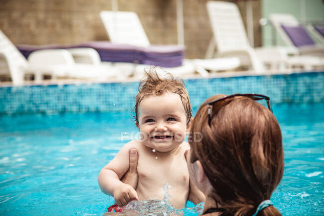 Вид сзади матери в бассейне, держащей своего маленького сына, Болгария — стоковое фото