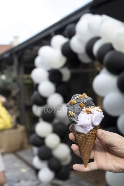 Mão humana segurando um gergelim preto e sorvete violeta cone — Fotografia de Stock
