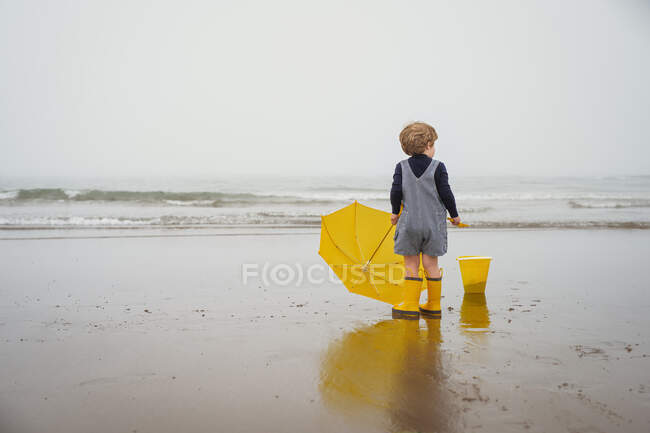 Хлопчик стоїть на пляжі з парасолькою, Бедфорд, Нова Шотландія, Канада. — стокове фото