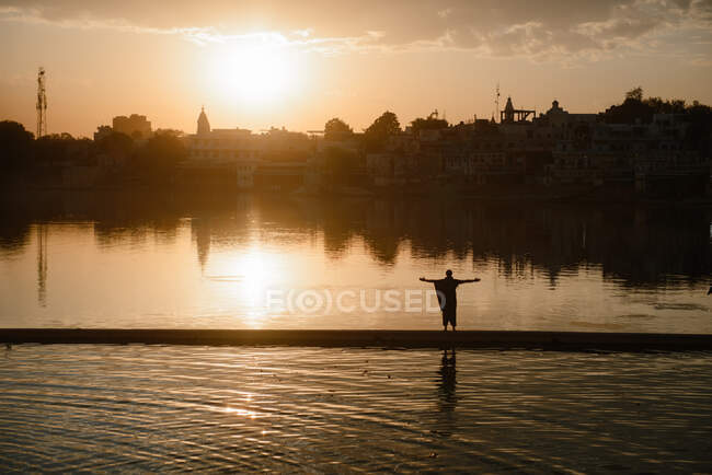Silueta de un hombre de pie junto a un lago al atardecer, Pushkar, Rajastán, India - foto de stock