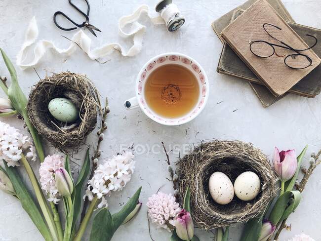 Uova di Pasqua in nidi con tè, fiori e libri — Foto stock