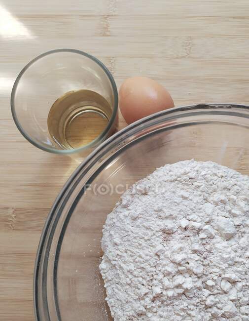 Tigela de farinha com um ovo e um copo de vinho branco — Fotografia de Stock