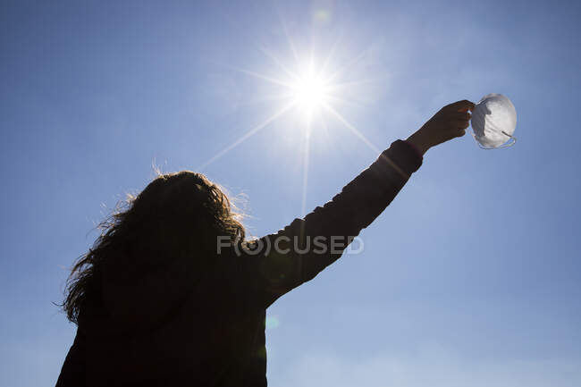 Rear view of woman standing outdoors taking face mask off — Stock Photo