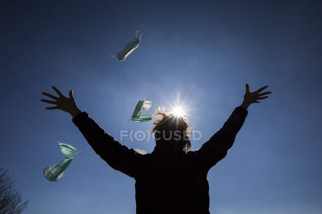 Rear view of a woman standing outdoors throwing face masks in air — Stock Photo