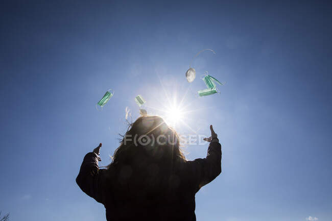 Rückansicht einer im Freien stehenden Frau, die Gesichtsmasken in die Luft wirft — Stockfoto