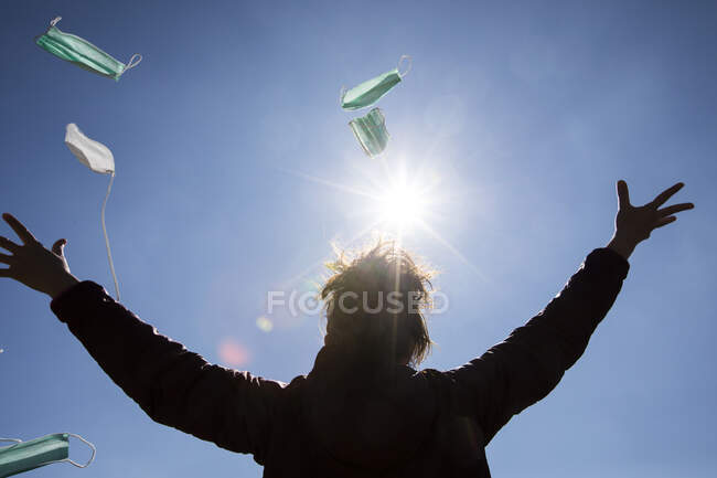 Visão traseira de uma mulher de pé ao ar livre jogando máscaras no ar — Fotografia de Stock