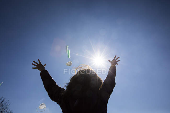 Rückansicht einer im Freien stehenden Frau, die Gesichtsmasken in die Luft wirft — Stockfoto