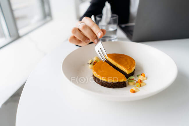 Close-up of a businesswoman eating sea buckthorn cheesecake while working — Stock Photo