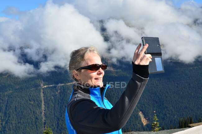 Retrato de uma mulher sorridente tirando uma selfie nas montanhas, Whistler, British Columbia, Canadá — Fotografia de Stock