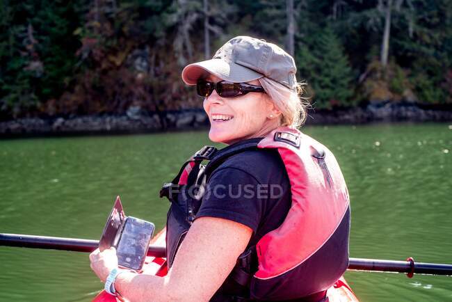 Donna sorridente in kayak con in mano un cellulare, Brentwood Bay, Columbia Britannica, Canada — Foto stock