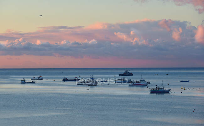 Самолет пролетает над рыбацкими лодками, стоящими на якоре в море на восходе солнца, Мальта — стоковое фото