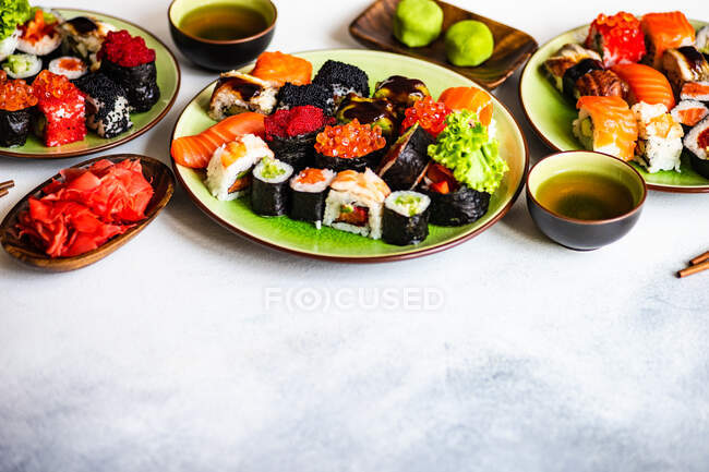 Set de Sushi con varios sashimi, rollos de sushi y té servido en pizarra de piedra - foto de stock
