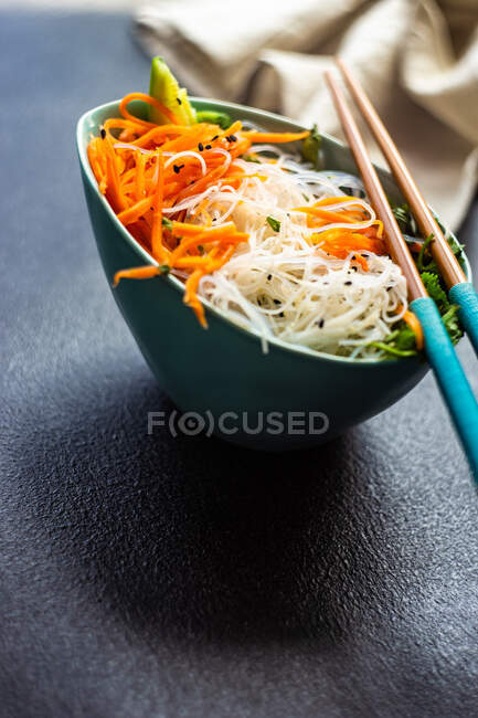 Bol en céramique avec salade de légumes et pâtes servies sur table en pierre avec baguettes — Photo de stock