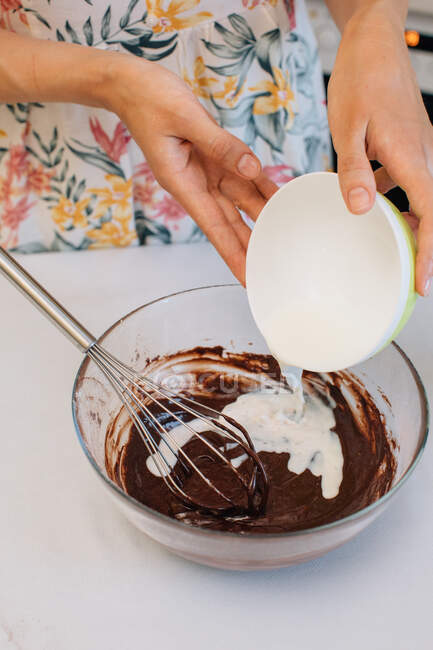 Woman adding milk to chocolate cake mixture — Stock Photo
