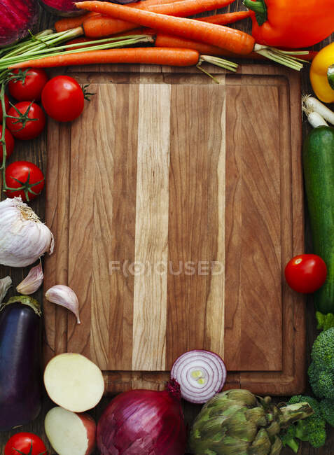 Tagliere di legno circondato da frutta e verdura fresca — Foto stock