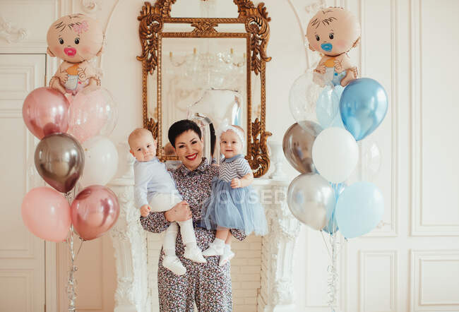 Retrato de una mujer sonriente sosteniendo a sus nietos gemelos en su primer cumpleaños - foto de stock