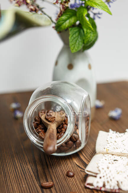 Tarro de vidrio lleno de granos de café tostados junto a un jarrón de flores - foto de stock