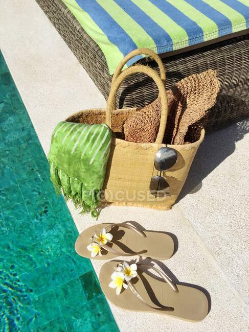 Chanclas y una cesta con accesorios de verano junto a una piscina - foto de stock