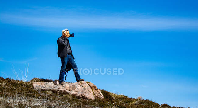 Man standing on a rock taking a photo, Highlands, Scotland, UK — Stock Photo