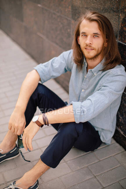 Handsome man sitting on the ground leaning against a wall — Stock Photo