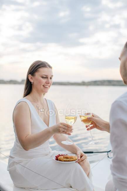 Coppia sorridente seduta su uno yacht a brindare con un bicchiere di vino bianco, Russia — Foto stock