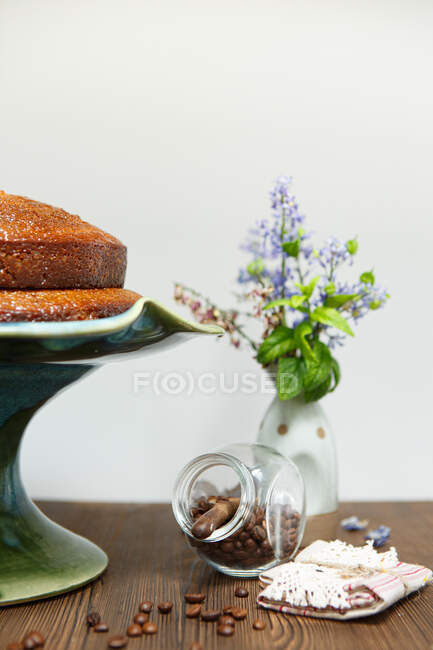 Pastel de café en una tarta junto a granos de café tostados y un jarrón con flores - foto de stock
