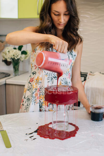 Woman pouring glaze over a home made red velvet chocolate cake — Stock Photo