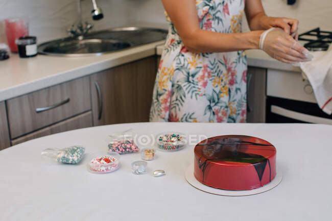 Женщина, стоящая на кухне и украшающая шоколадный красный бархатный торт — стоковое фото