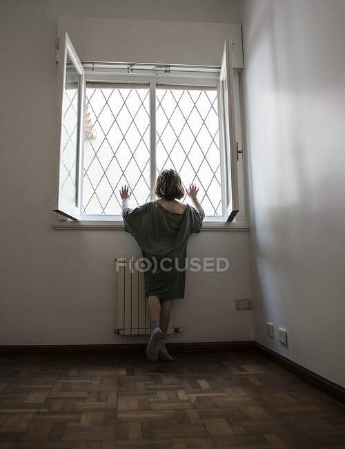 Вид ззаду дівчини в пастці в кімнаті, яка дивиться через вікно — стокове фото