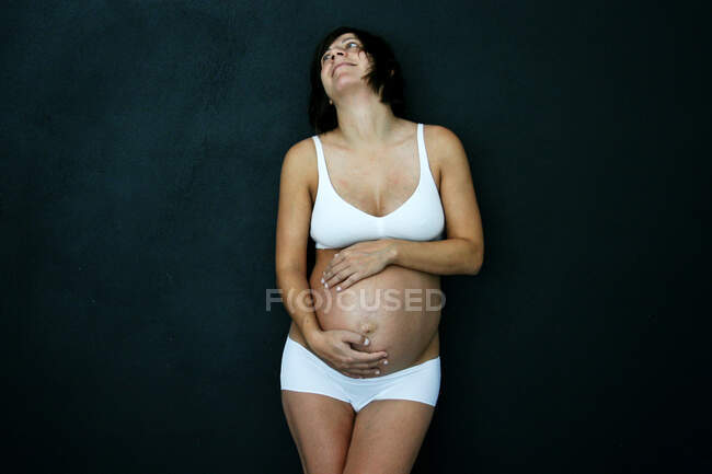 Mujer embarazada en ropa interior acunando su bulto - foto de stock