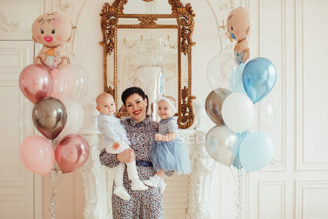 Portrait of a smiling woman holding her twin grandchildren on their 1st birthday — Stock Photo