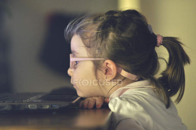Chica sentada en una mesa mirando la pantalla de una computadora - foto de stock