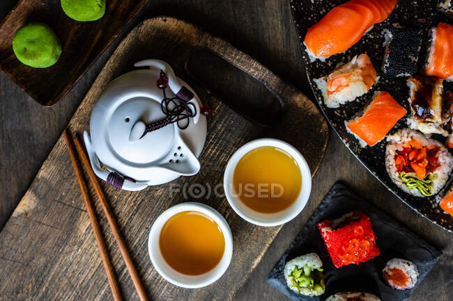 Platos de surtidos rollos de sushi maki y sushi nigiri en una mesa con té verde - foto de stock