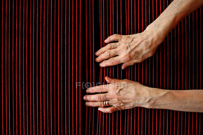 Las manos de la mujer anciana tocando hilos de lana roja - foto de stock