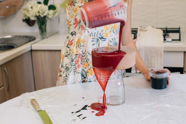 Mulher derramando esmalte sobre uma casa feita bolo de chocolate de veludo vermelho — Fotografia de Stock