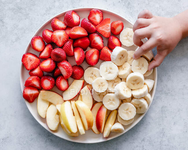 Mano del bambino che raggiunge per la banana su un piatto di frutta snack — Foto stock