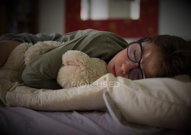 Menina cochilando em uma cama com seu ursinho de pelúcia — Fotografia de Stock