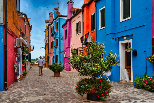 Hombre caminando por casas multicolores, Burano, Venecia, Véneto, Italia - foto de stock