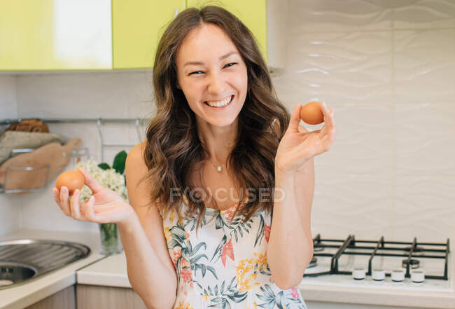 Happy woman standing in a kitchen holding two eggs — Stock Photo
