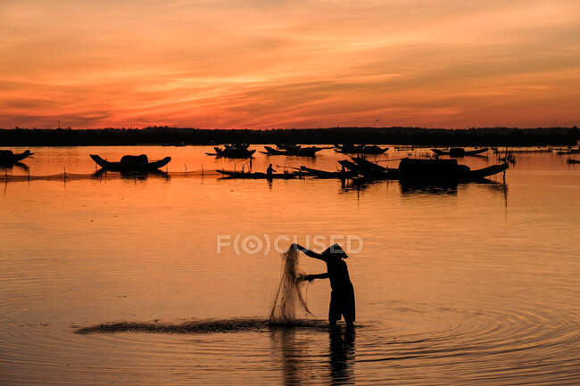 Silhouette di un pescatore in piedi nel fiume con una rete da pesca all'alba, Vietnam — Foto stock