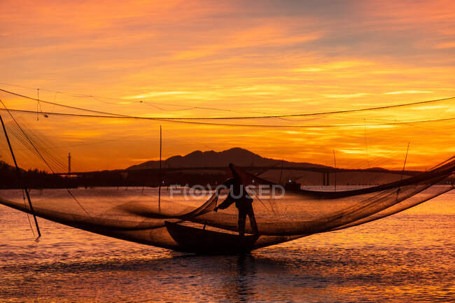 Silhouette d'un pêcheur vérifiant ses filets au lever du soleil, Vietnam — Photo de stock