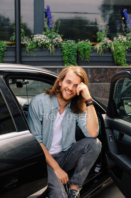 Retrato de un hombre sonriente sentado en un coche con la puerta abierta - foto de stock