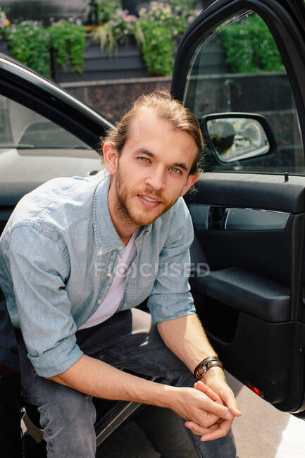 Retrato de un hombre sentado en un coche con la puerta abierta - foto de stock