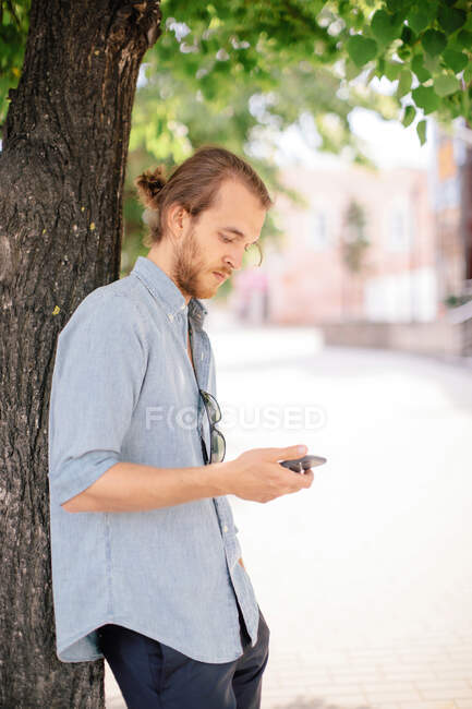 Mann lehnt an einem Baum und blickt auf sein Handy, Russland — Stockfoto