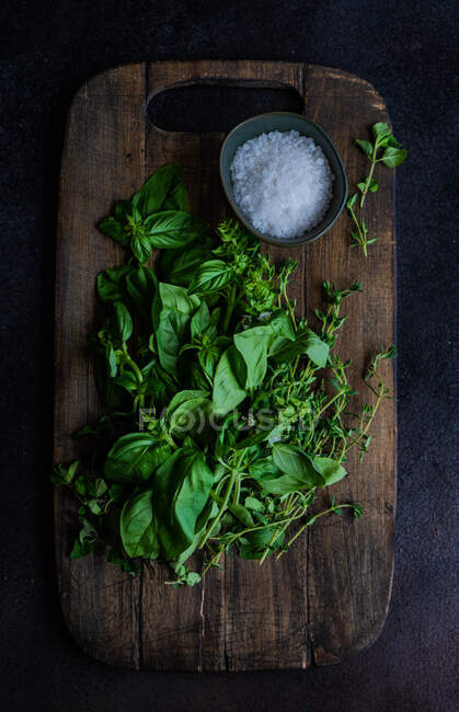 Basil, thyme, oregano and salt on a wooden chopping board — Stock Photo