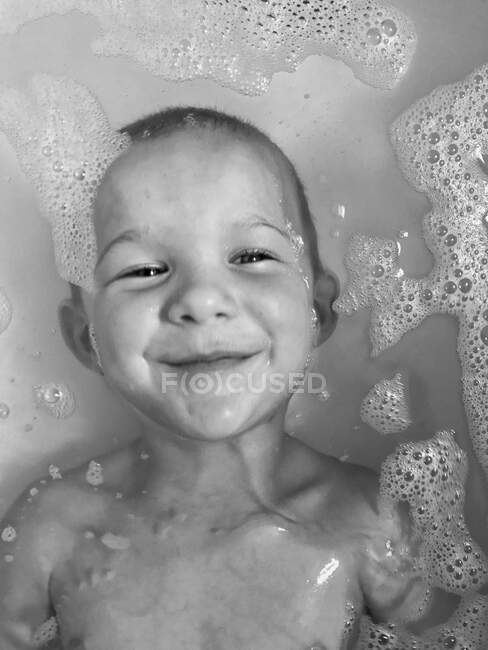 Sonriente chico acostado en el baño y mirando a la cámara - foto de stock