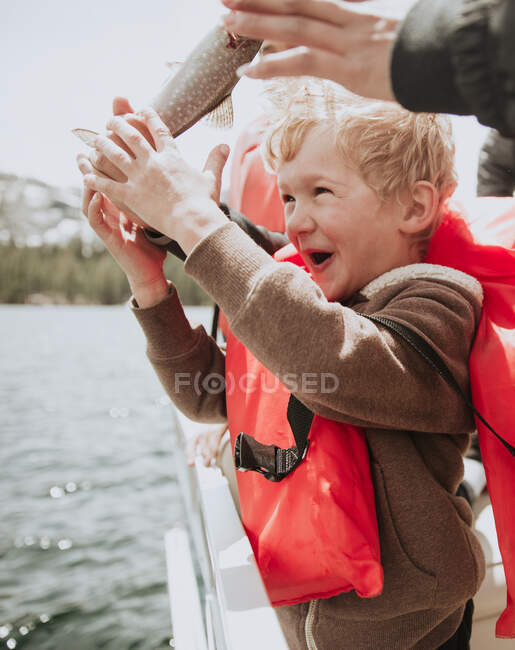 Junge steht auf einem Boot mit einem frisch gefangenen Fisch, USA — Stockfoto