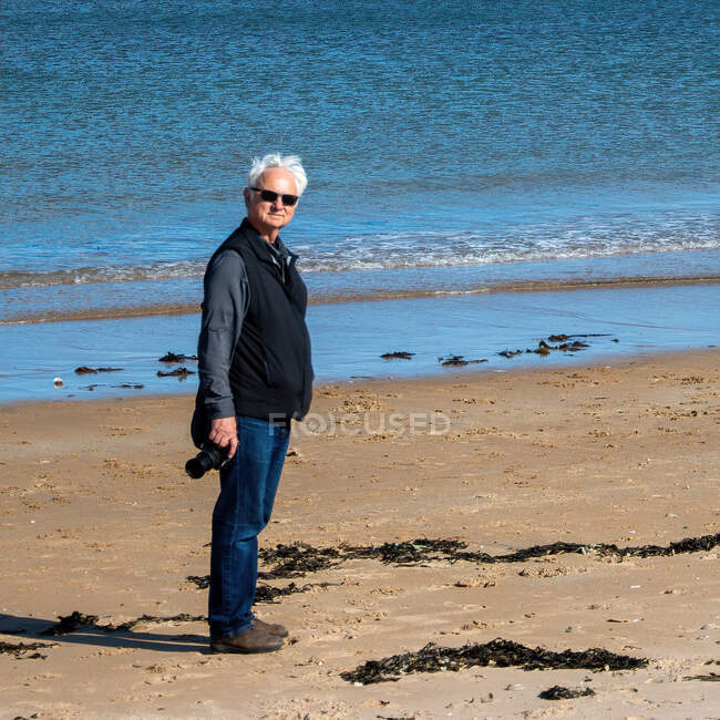 Чоловік стоїть на пляжі з камерою на острові Скай (Шотландія, Англія). — стокове фото