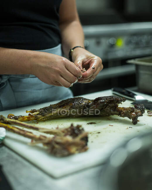 Cook cleaning meat off cooked chicken bones — Stock Photo